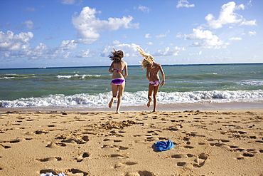 Two pre-teen girls undressing as they run into the water at Paia Beach, Maui, Hawaii.