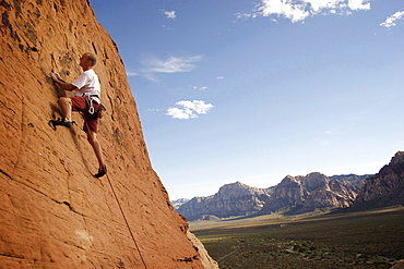 A rock climber ascends a red rock face in Nevada.