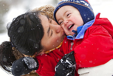 A two year old boy plays in a snowy field during a snowstorm in a red snowsuit with his mother in a park, Fort Collins, Colorado.