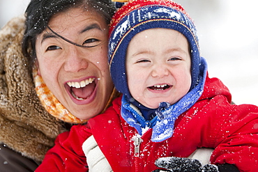 A two year old boy plays in a snowy field during a snowstorm in a red snowsuit with his mother in a park, Fort Collins, Colorado.