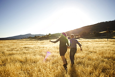 Couple hold hands and run together in an open field.