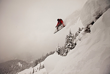 A snowboarder jumps off a cliff into powder in Colorado.