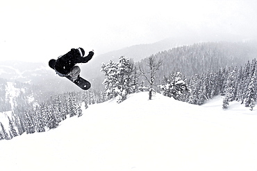 A man on a snowboard flies through the air after hitting a jump.