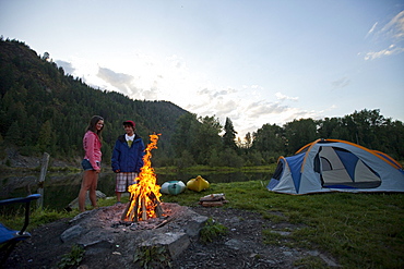 Young adult couple camping with a camp fire and kayaks on a beautiful summer evening.