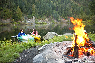 Young adult couple camping with a camp fire and kayaks on a beautiful summer evening.