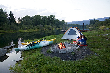 Young adult couple camping with a camp fire and kayaks on a beautiful summer evening.