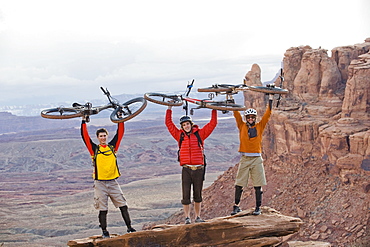 Three young men hold their bikes over their heads on the Amasa Back Trail, Moab, UT.