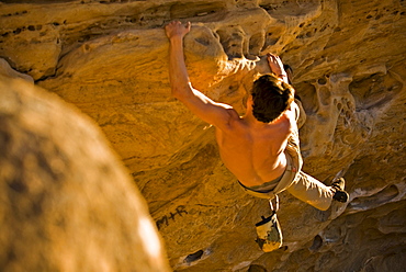 A young man rock climbs a boulder problem in Santa Barbara, CA.