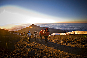 A team of hikers approach the summit of Mt. Kilimanjaro at sunrise after trekking six hours through the night.