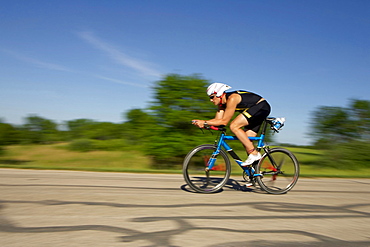 A male athelete training for a triathlon at a lake on a bike.