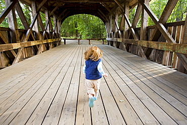 A little girl runs across a covered bridge.