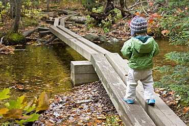 A young girl walks across hiking bridges in Grafton Notch State Park, Maine.