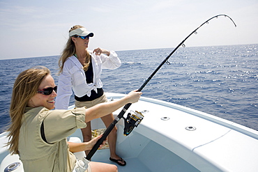 Two women are fishing on the bow of a boat with the rod bending on a catch.