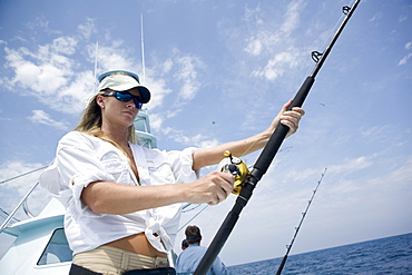 A blonde woman holds a fishing rod while watching for a sailfish to bite.