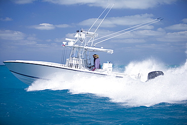 A fishing boat speeds through the blue surf spraying white water.