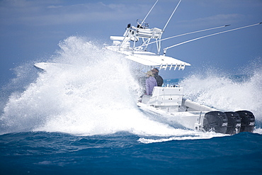 A fishing boat speeds through the blue surf spraying white water.