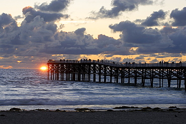 The last rays of sun penetrate the clouds behind Crystal Pier at sunset; San Diego, CA.