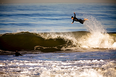 A male surfer jumps over the top of a breaking wave in Ventura, California.