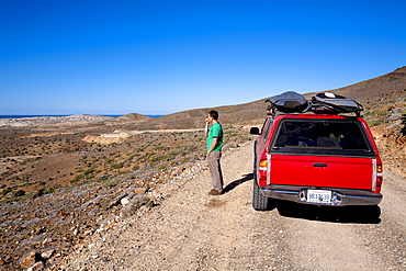 A male surfer looks out over the desert to check the surf in Baja, Mexico.