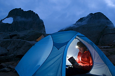 Man reading guidebook by headlamp in tent, Bugaboo Provincial Park, Radium, British Columbia, Canada.