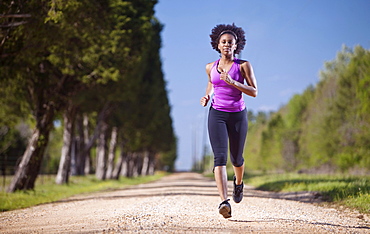 A woman runs on a dirt road lined with trees.