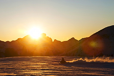 A athletic young man snowmobiling at sunset in Cooke City, Montana.