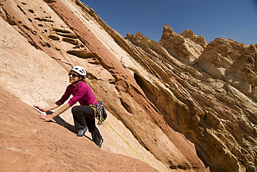 A woman rock climbing up a colorful sandstone slab at the Reef, San Rafael Swell, Green River, Utah.