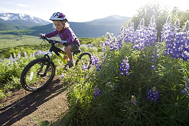 A young girl mountain biking past wildflowers on the Lupine Loop Trail in Crested Butte, Colorado.