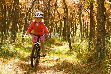 A young girl mountain biking on a trail through Gambrel Oak in orange fall color, La Plata Mountains, Mayday, Colorado.