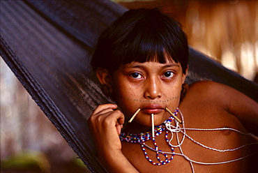 Yanomami Indian girl with sticks at the corners of her mouth and just below her lower lip and bead necklaces lies in a hammock in her village in the Amazonian Forest in southern Venezuela.