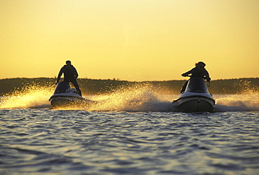 Two jet skis in open water at sunset.