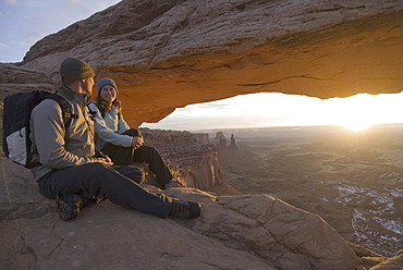 Man and woman hiking by rock arch.