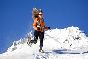 Woman runs with snowshoes in snow.