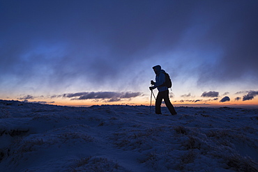 Silhouette of hiker on wintry summit of Corn Du at dawn, Brecon Beacons national park, Wales