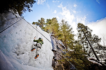 An adventurous female wearing a green jacket climbs a frozen icy waterfall near Pemberton, British Columbia, Canada.