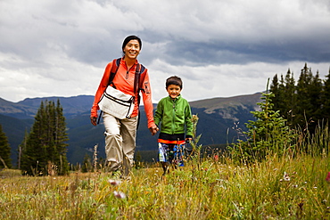 A mid-thirty year old Japanese-American mother walks with her five year old son through a meadow of wild flowers on the way to Lower Crystal Lake, Colorado.