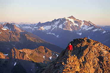 A hiker walks a rocky ridge with Mount Shuksan in the background, North Cascades National Park, Washington, United States