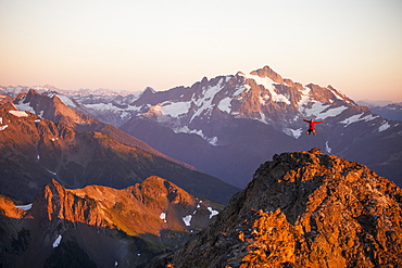 A hiker jumps into the air from a rocky ridge in the North Cascade Mountains with Mount Shuksan in the background, North Cascades National Park, Washington, United States