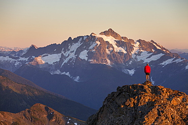 A hiker stands on a rocky ridge in the North Cascade Mountains with Mount Shuksan in the background, North Cascades National Park, Washington, United States