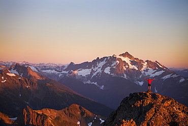 A hiker stands on a rocky ridge in the North Cascade Mountains with Mount Shuksan in the background, North Cascades National Park, Washington, United States