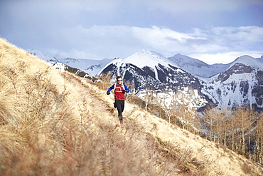 Adult male trail running through a grassy trail high in the mountains above Telluride Colorado on a beautiful spring afternoon, Telluride, Co, USA