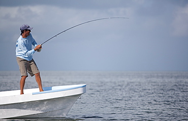 fly rod bends as a fisherman reels in while standing on the bow of his boat, San Pedro, Belize