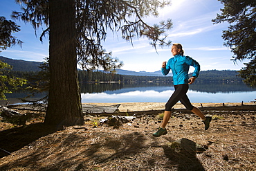 A female trail runner running next to Payette Lake in Ponderosa State Park, McCall, Idaho in the fall, Ponderosa State Park, McCall, Idaho, USA