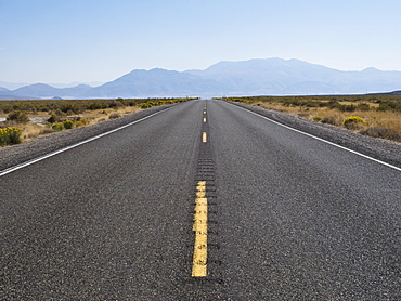 Desolate road (Nevada 140) in Northern Nevada leads to a hazy mountain in the distance.