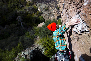 A male climber in an orange beanie and multicolored shirt climbs Family Jewel (5.10d) on Mount Gorgeous in Malibu Canyon State Park in Malibu, California.  Family Jewel is a very popular sport climb in Malibu Canyon.