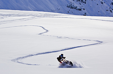 A women riders her snowmobile through a powdery field leaving the evidence of her turns behind her.