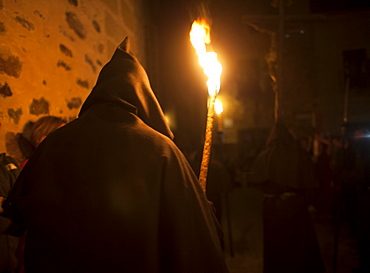 A penitent dressed as a Benedictine monk holds a torch at the procession of the Black Christ of Santa Maria during Easter Holy Week inside of the Cathedral of Caceres, Extremadura, Spain