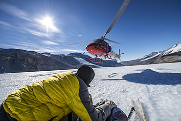 A scientist holds equipment while a helicopter lands next to him on the Taylor Glacier, Antarctica.