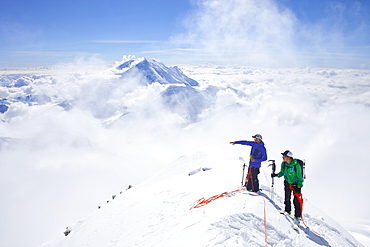 High Mountain Rangers Tom Ditola and David Weber are taking a rest on the West Rib on Mount McKinley, Alaska. Mount Hunter in the background. They are above the clouds in blue sky and the sun is shining.     Mount McKinley, native name Denali, is the highest mountain peak in North America, with a summit elevation of 20,321 feet (6,194 m) above sea level. At some 18,000 feet (5,500 m), the base-to-peak rise is considered the largest of any mountain situated entirely above sea level. Measured by topographic prominence, it is the third most prominent peak after Mount Everest and Aconcagua. Located in the Alaska Range in the interior of the U.S. state of Alaska, McKinley is the centerpiece of Denali National Park and Preserve.    Every climbing season High Mountain Rangers of the Denali National Park Service are called to help climbers in need. If possible the patient is brought down to base camp on foot, only in life threatening conditions a helicopter is called to evacuate the patient to a hospital in Anchorage.