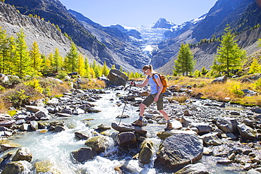 A female hiker crossing a river in the Swiss Alps. In the background is the Ried glacier. This region of Wallis, close to Zermatt, is a paradise for outdoor enthusiasts like climbers, alpinists, hikers, mountainbikers and nature lovers. The water is directly coming from the glacier, so very refreshing after an excercise.